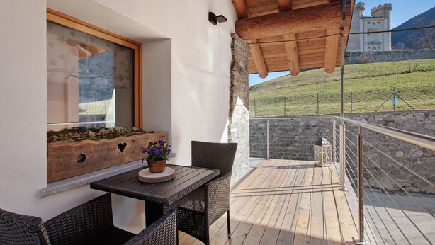 A balcony with a table, chairs, a potted plant, and a view of a castle. - Holiday Home 'Alpine A&S' with Mountain View, Wi-Fi and Air Conditioning (Aymavilles)