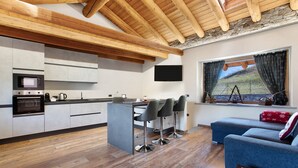 A modern kitchen with a central island, bar stools, a flat-screen TV, and a large window with curtains. - Holiday Home 'Alpine A&S' with Mountain View, Wi-Fi and Air Conditioning (Aymavilles)