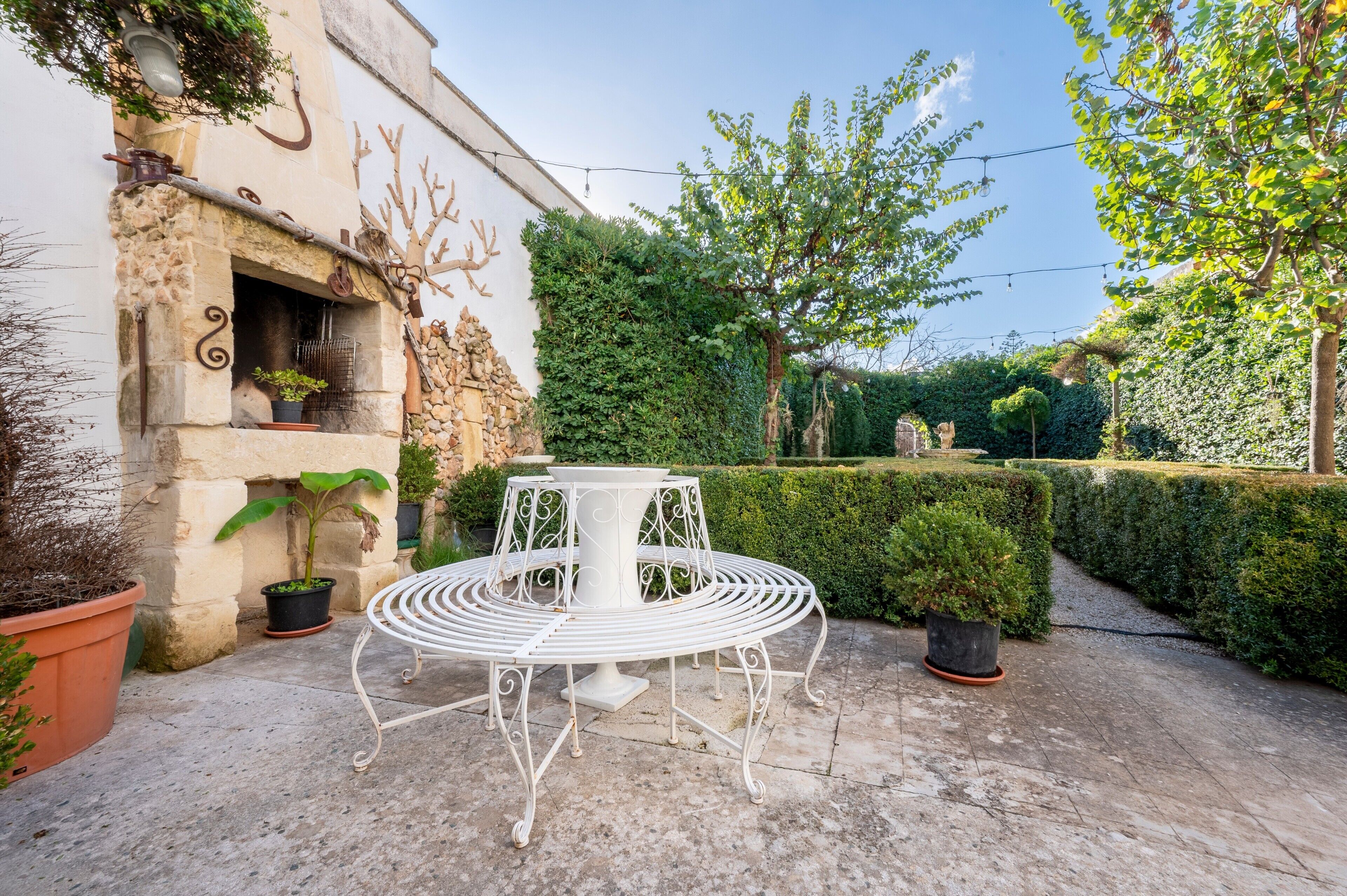 A courtyard with a white metal table and chairs, potted plants, and a stone wall.