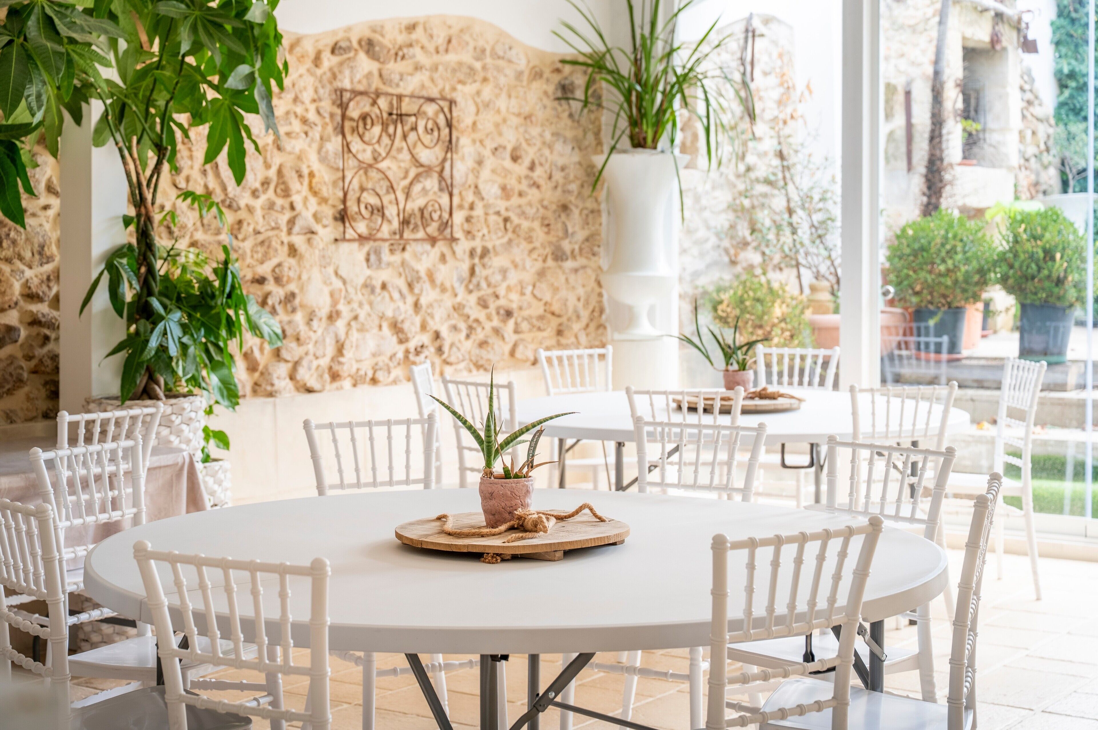 A round table with chairs, potted plants, and a stone wall with a mural.