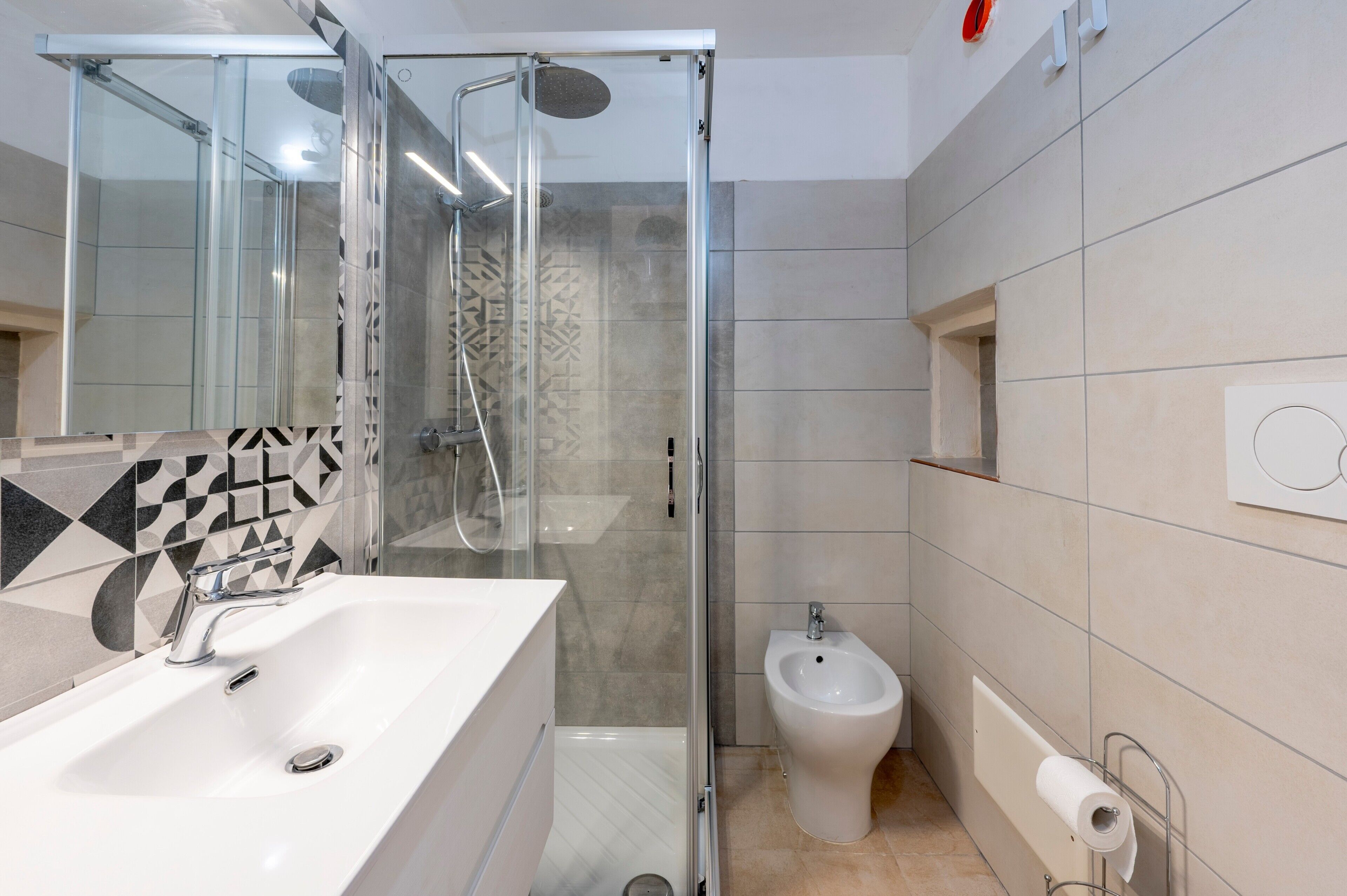 A bathroom with a glass-enclosed shower, a white sink, a bidet, and a toilet.