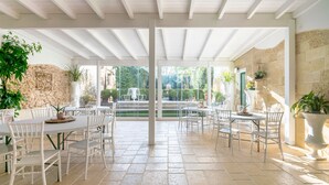 An outdoor patio with white tables and chairs, stone walls, and potted plants. - Room 'Palazzo Costantini - Girasole' with Shared Terrace, Wi-Fi and Air Conditioning (San Donato di Lecce)