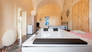 Una habitación con una bañera grande, una cama con colcha de diseño azul y blanco, una puerta de madera y una pared de piedra.