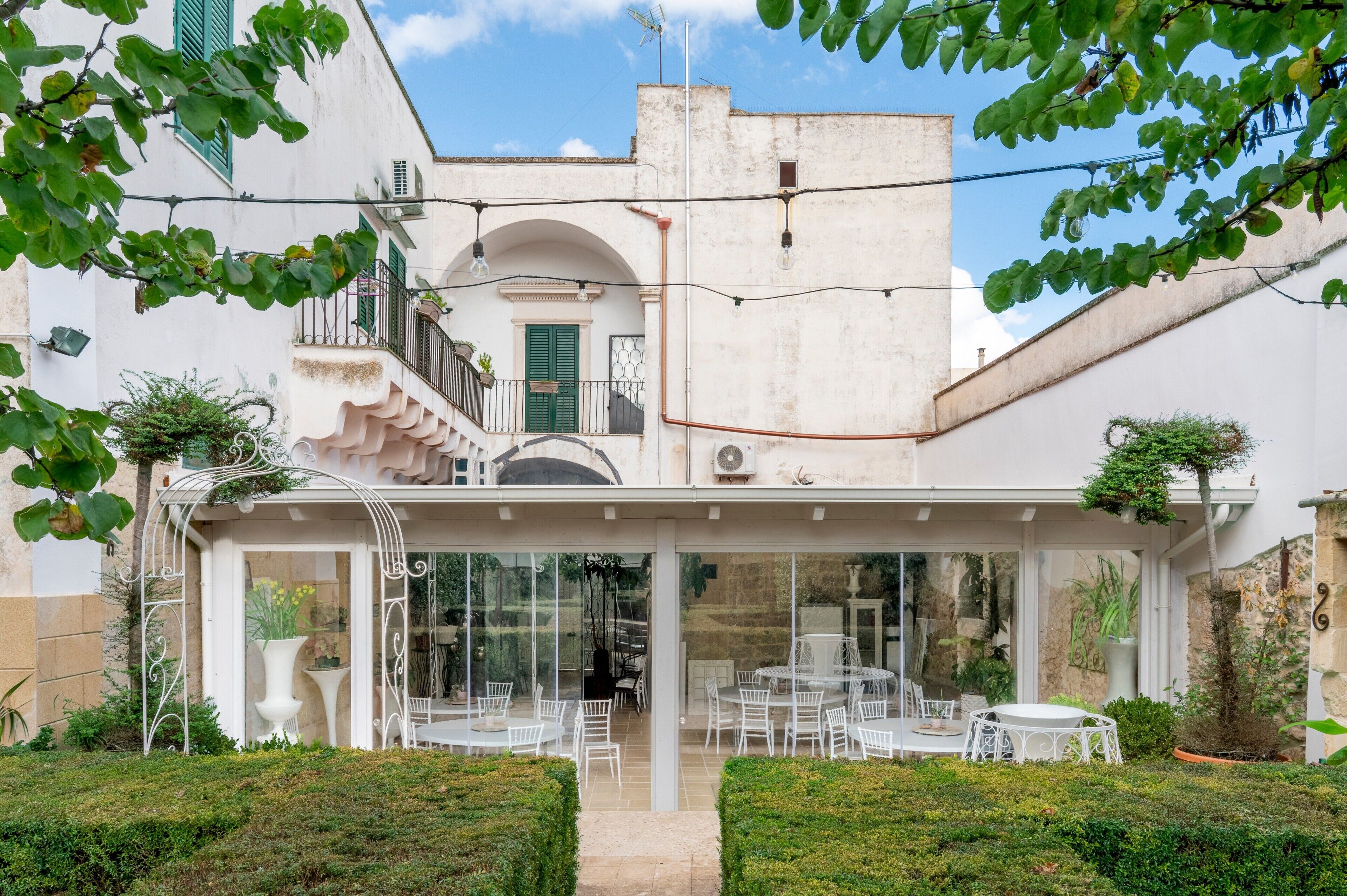 Un cortile con posti a sedere all'aperto, una zona pranzo vetrata e un edificio bianco con persiane verdi.
