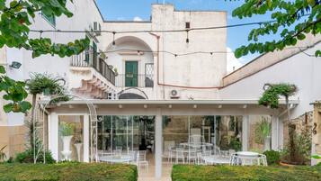 Un cortile con posti a sedere all'aperto, una zona pranzo vetrata e un edificio bianco con persiane verdi.