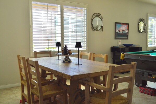 A dining area with a wooden table and chairs, a billiards table, and a window with blinds. - Resort Style Home- Pool Table- Walking Distance to Coachella Fest & Stagecoach (Indio)