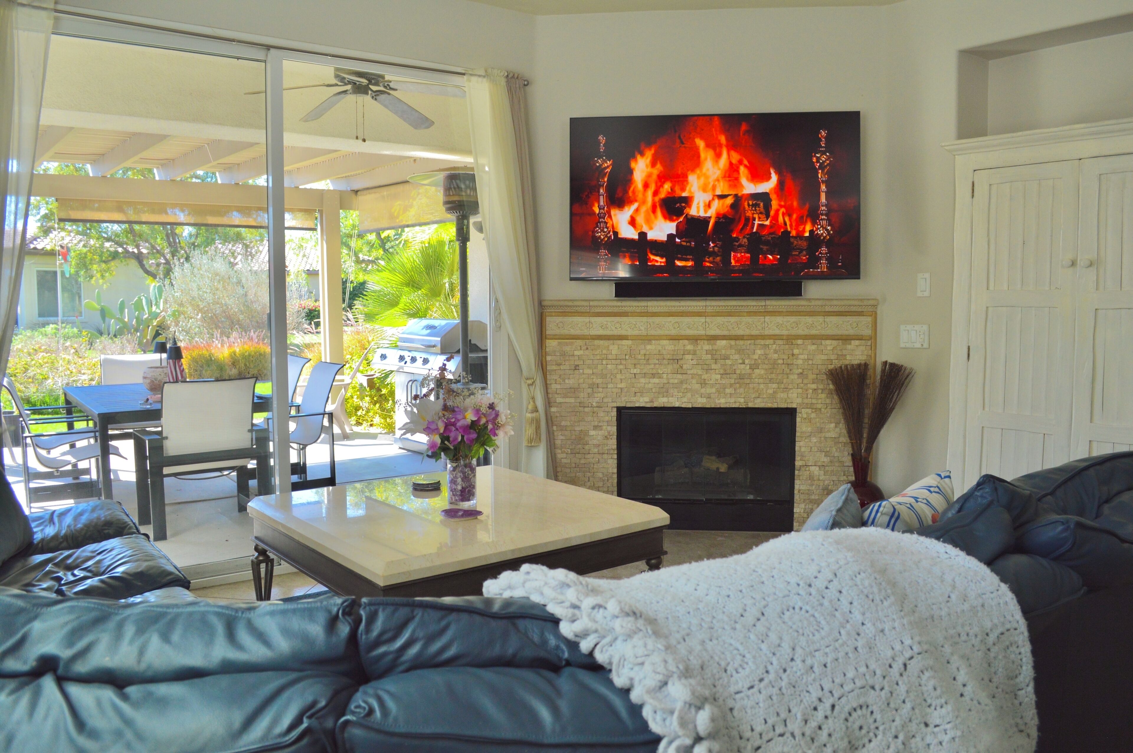 A living room with a fireplace, a television mounted above it, and a patio area with outdoor furniture.