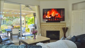 A living room with a fireplace, a television mounted above it, and a patio area with outdoor furniture. - Resort Style Home- Pool Table- Walking Distance to Coachella Fest & Stagecoach (Indio)