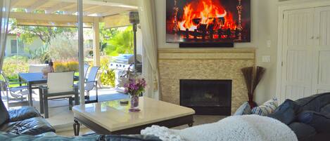 A living room with a fireplace, a television mounted above it, and a patio area with outdoor furniture.