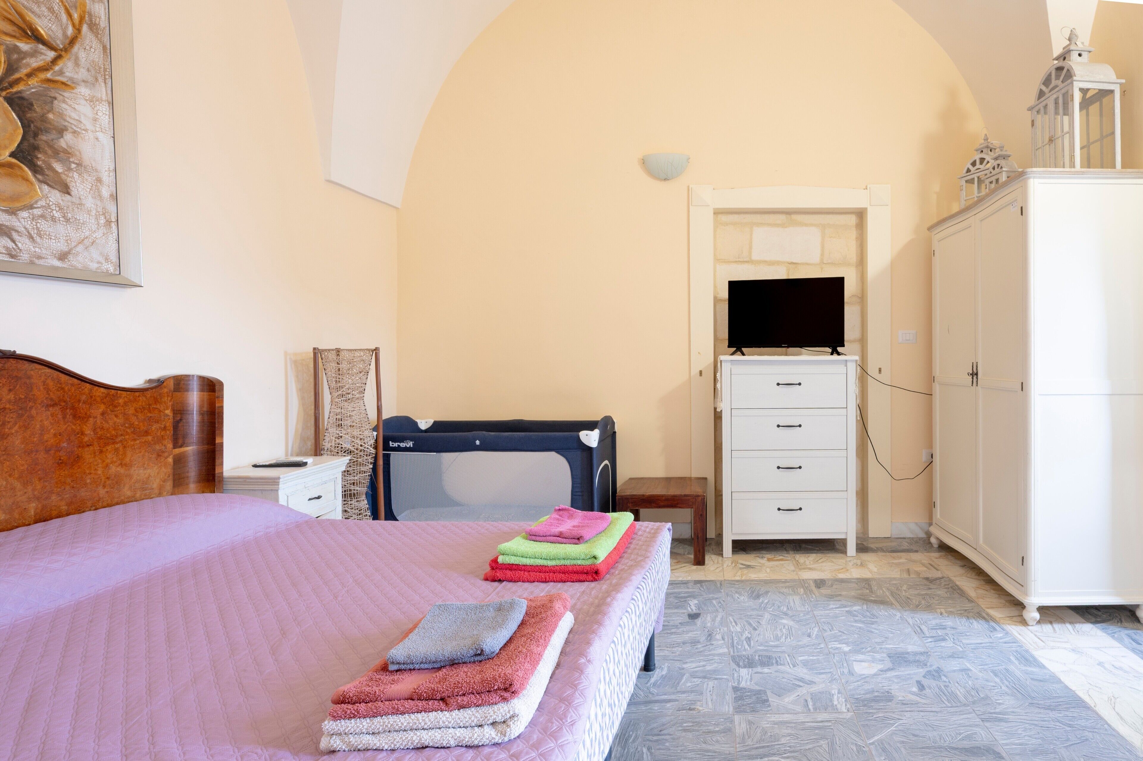Ein Schlafzimmer mit Bett, Babybett, Fernseher, Kleiderschrank und einem Bild an der Wand.