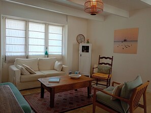 A living room with a sofa, a wooden coffee table, a chair, a small table with a vase, a clock, and a picture on the wall.