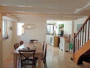 Et spiseområde med et træbord og stole, en hængende lampe samt et køkken i baggrunden.
