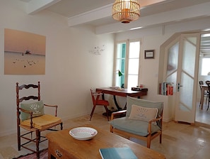Et hyggeligt værelse med et træbord, to stole, et skrivebord med en lampe, et vindue med persienner og en dør med et skærmpanel.