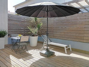 Una terrazza con tavolo, sedie, una pianta in vaso e un ombrellone grande.