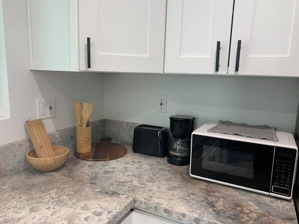 Una cocina con armarios blancos, un microondas, una cafetera y utensilios de madera sobre una encimera con motas.