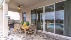 An outdoor patio with a table and chairs, a grill, and a pool area with glass doors. - 284 Encore at Reunion (Kissimmee)