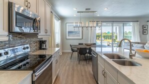 A modern kitchen with stainless steel appliances, a dining area with a large island, and a view of the outdoors. - 284 Encore at Reunion (Kissimmee)