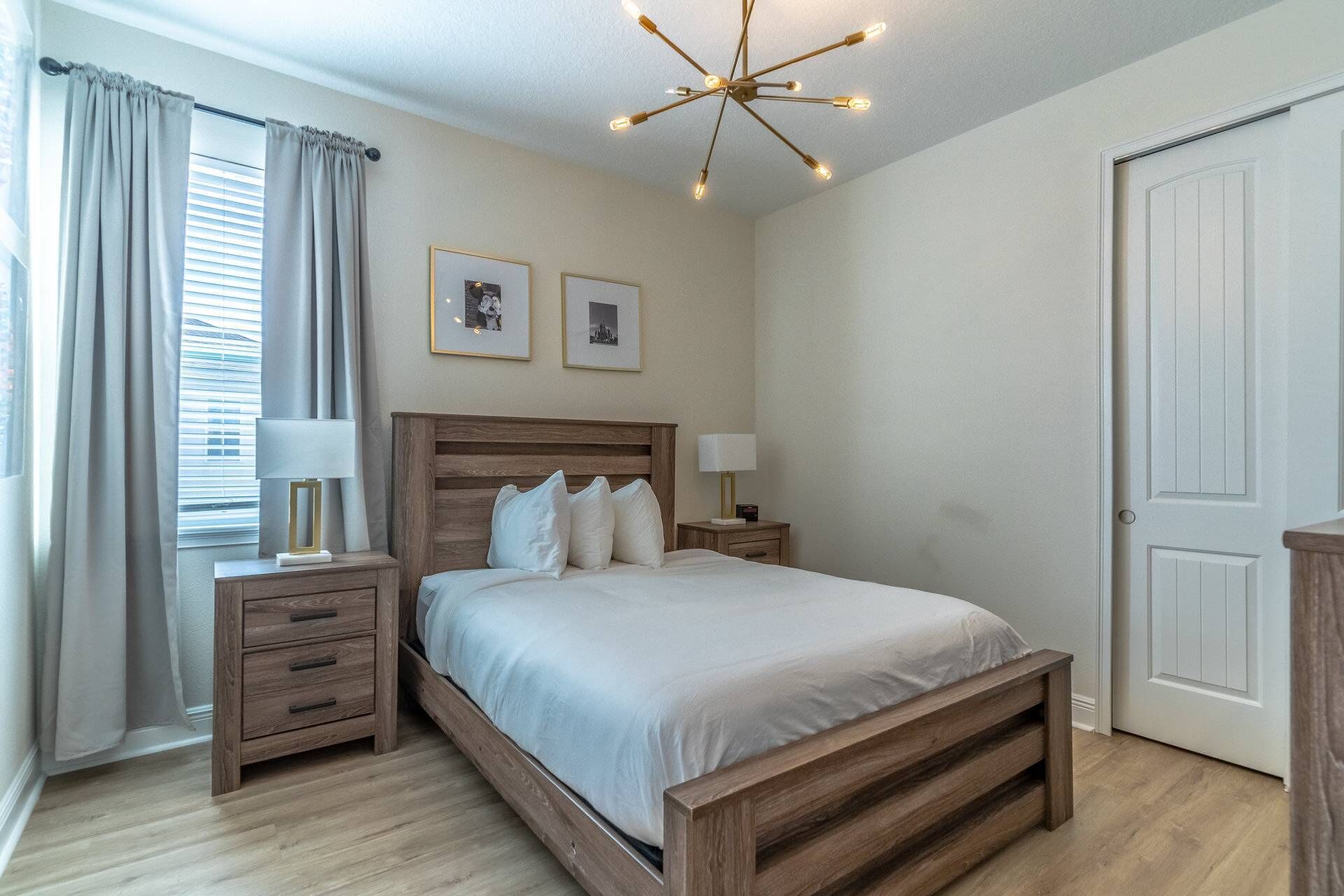 A bedroom with a wooden bed, two bedside tables with lamps, a ceiling light fixture, and two framed pictures on the wall.