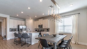 A modern kitchen with white cabinets, stainless steel appliances, and a central island with bar stools. - 284 Encore at Reunion (Kissimmee)