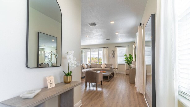 A spacious living area with a sofa, coffee table, and a large mirror. There is a potted plant and a framed picture on the wall. - 284 Encore at Reunion (Kissimmee)