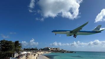 An airplane flying over a beach with clear skies and a few clouds.
