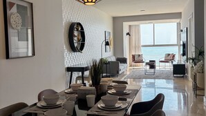A modern dining area with a long table set for a meal, a large pendant light, and a view of the ocean through large windows. - Departamento de lujo Yoo-Panamá 34B  (Panama City)