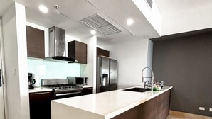 A modern kitchen with a central island, stainless steel appliances, and a dark backsplash. - Departamento de lujo Yoo-Panamá 34B  (Panama City)