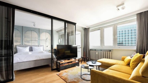 A modern hotel room with a bed, a sofa, a TV, and a view of the city. - Central Panorama Apartment | Chmielna 35 (Warszawa)