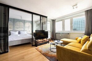 Ein modernes Hotelzimmer mit Bett, einer Couch, einem Fernseher und Blick auf die Stadt.