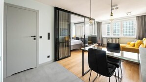 A modern hotel room with a sliding door leading to a bedroom, a dining area with a table and chairs, and a large window with curtains. - Central Panorama Apartment | Chmielna 35 (Warszawa)