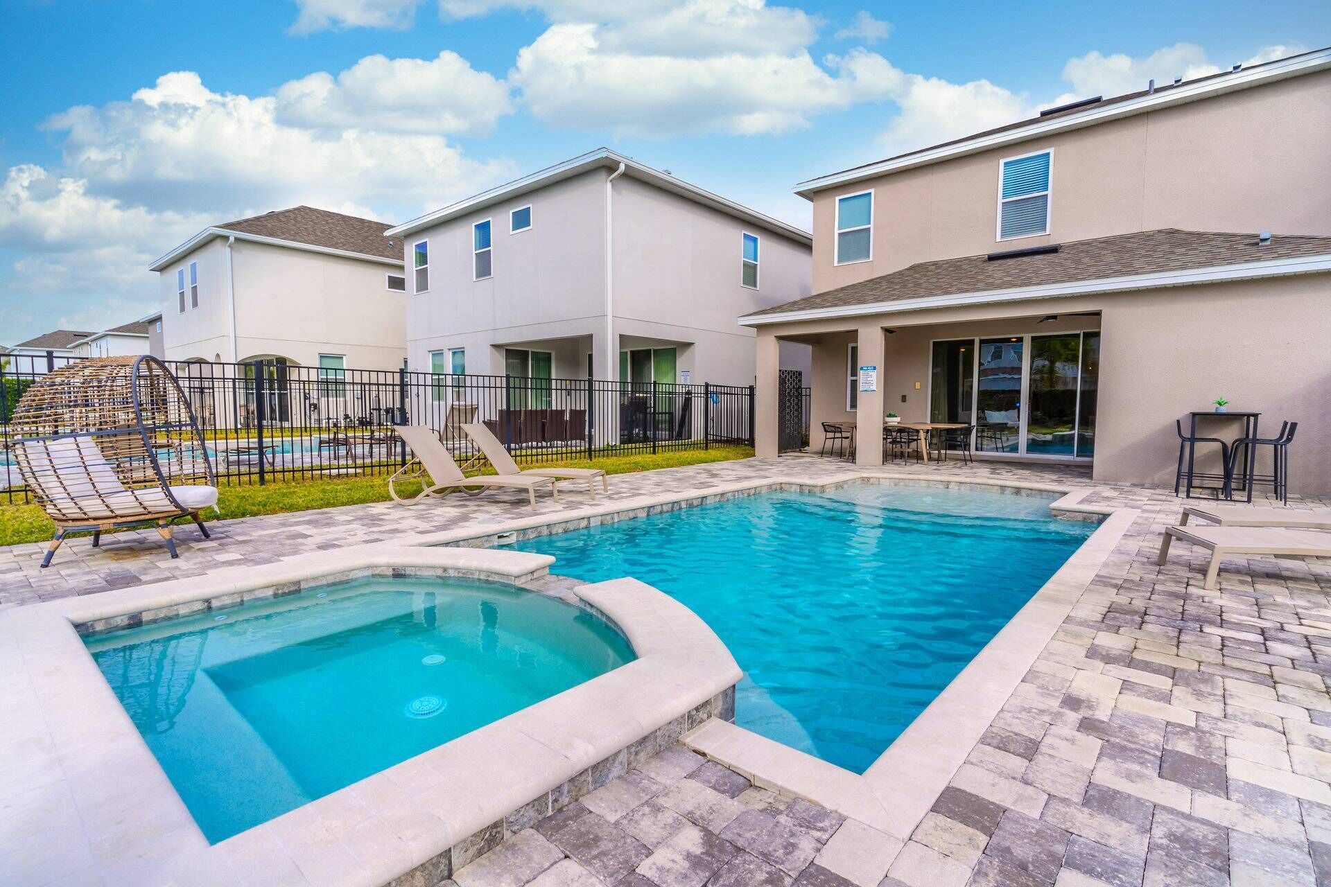 A residential pool area with a hot tub, lounge chairs, and a patio table.