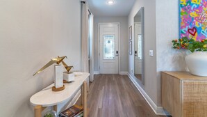 Un corridoio con una porta bianca, un tavolino consolle bianco con oggetti decorativi e un quadro astratto colorato appeso alla parete.