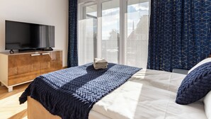 A hotel room with a bed, a TV on a wooden dresser, and a window with curtains. - Mostek Sapphire Navy Studio (Gdansk)