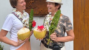 Two people holding coconuts and flowers in front of a wooden sign with the text "Caa Inn". - Mandhoo Inn (Mandhoo)