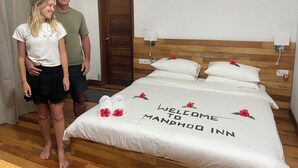 A hotel room with a bed, a wooden headboard, and a door. - Mandhoo Inn (Mandhoo)