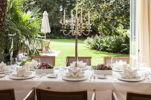 A table set for a formal outdoor dining experience with a view of a well-maintained garden and a candelabra centerpiece. - Mignon (Merano)