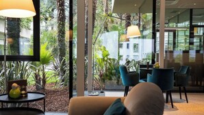 A modern hotel room with large windows, a dining area with blue chairs, and a small table with a lamp. - Mignon (Merano)