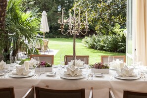 Une table dressée pour un repas élégant en plein air, avec vue sur un jardin bien entretenu et agrémentée d’un chandelier en guise de centre de table.