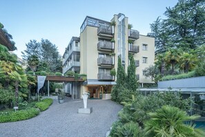 Ein modernes Mehrgeschosshaus mit Balkonen, einer überdachten Eingangsparte und einem begrünten Innenhof mit Pflanzen und einem Weg.