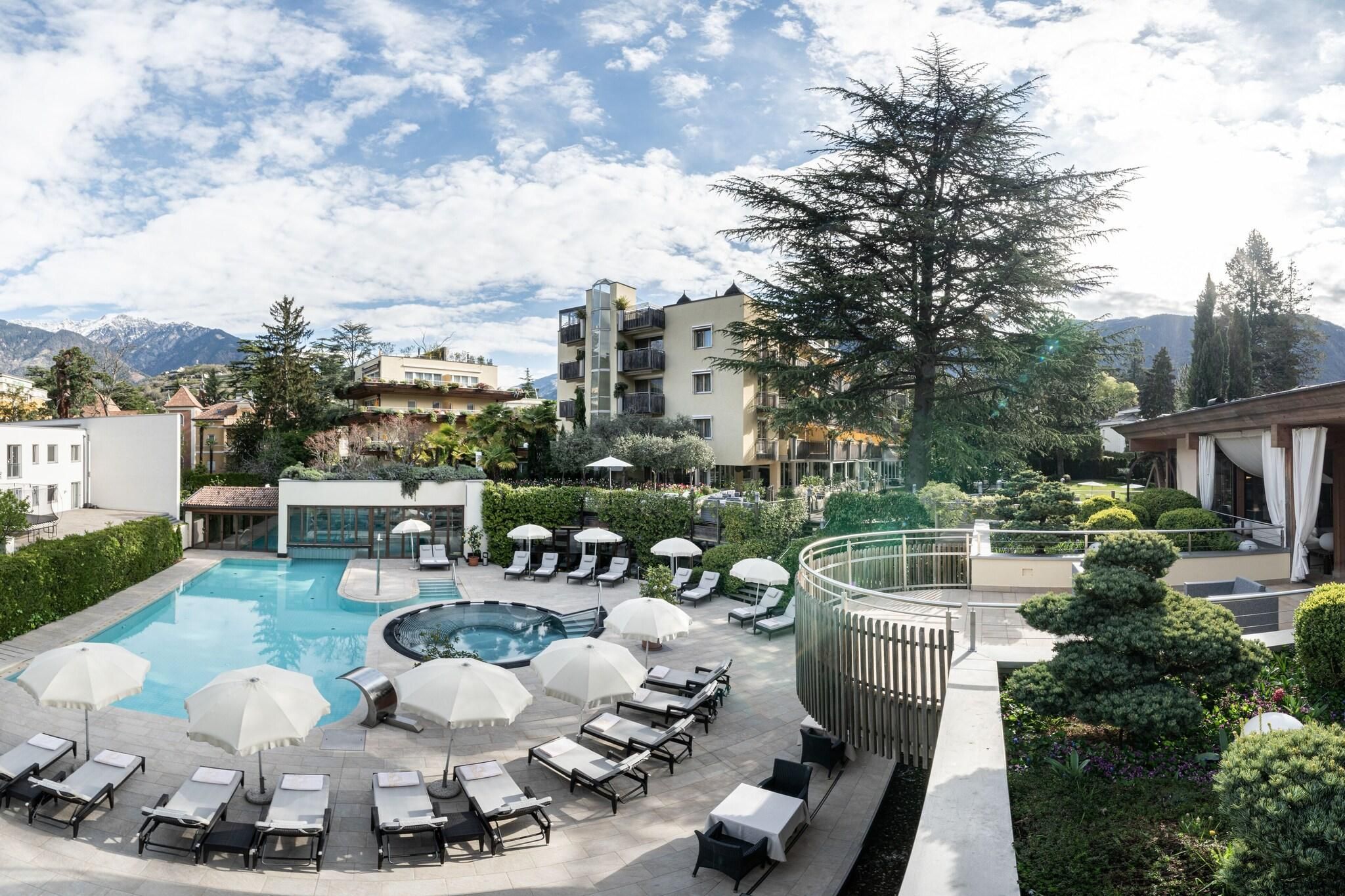 Área de piscina en la azotea con sillones de descanso y sombrillas, rodeada de vegetación y vistas a un paisaje montañoso.