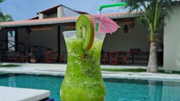 A green cocktail with a kiwi slice and a straw, placed on a wooden table by a pool.