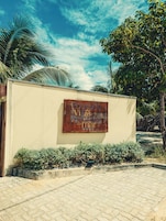 Letrero que indica 'Villa Recanto do mar', con entrada pavimentada y vegetación tropical.