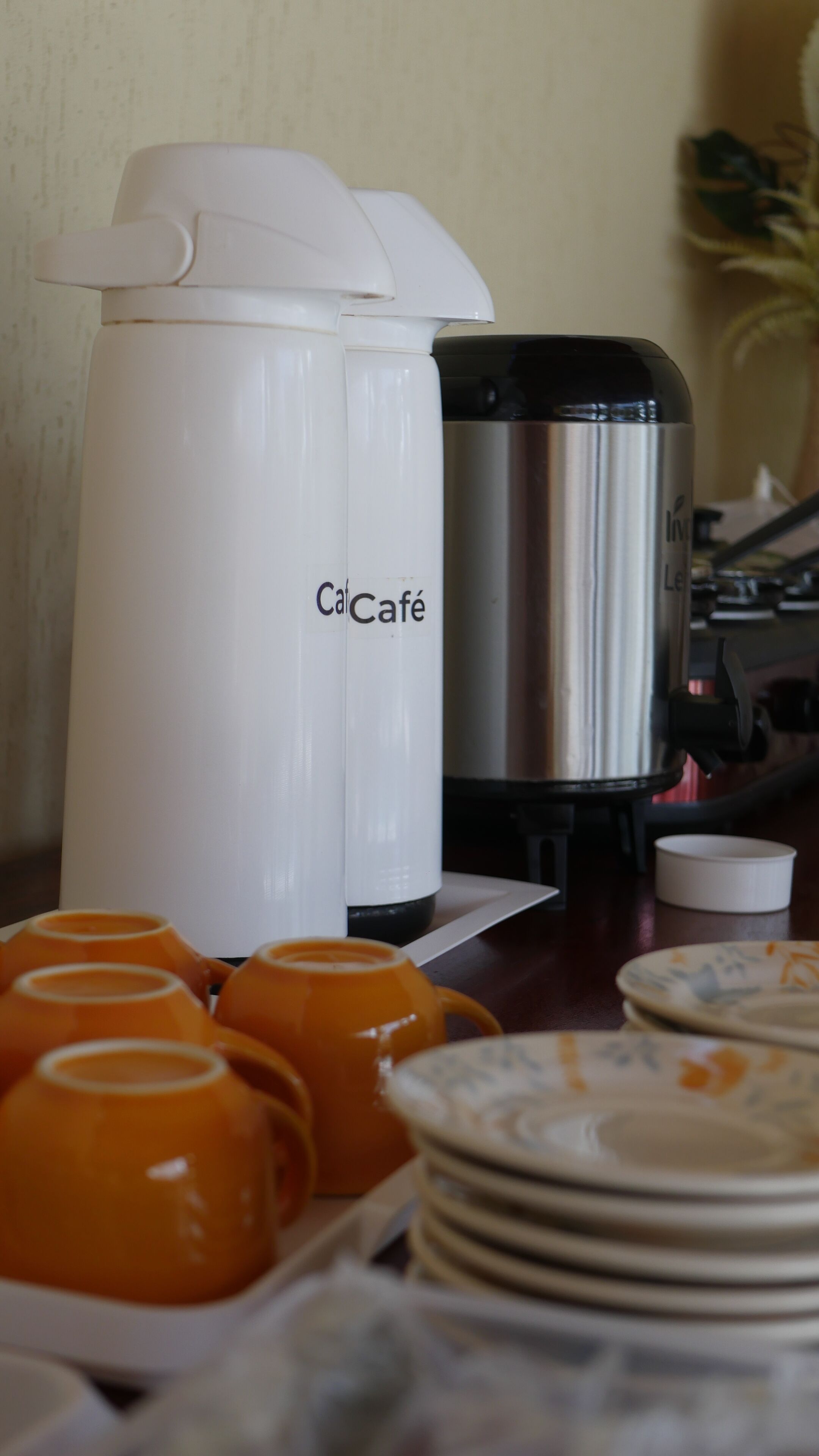 Eine Kaffeestation mit einer weißen Kaffeemaschine und einem Edelstahl-Kaffeekrug, orangefarbenen Tassen und weißen Tellern.