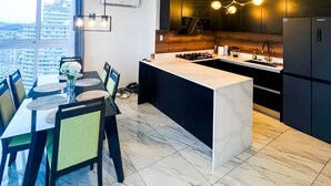 Una cocina moderna con una isla de mármol, armarios oscuros y vistas a la ciudad.