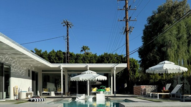 A swimming pool with lounge chairs and umbrellas, surrounded by a building with a covered patio area.