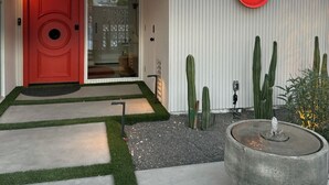 A modern house with a red door, a glass door, a red light, and cacti.