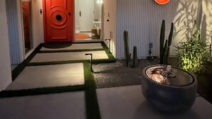 A modern house entrance with a red door, a pathway leading to a door, and a small outdoor fire feature.