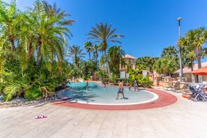 A pool area with palm trees, a water slide, and lounge chairs.