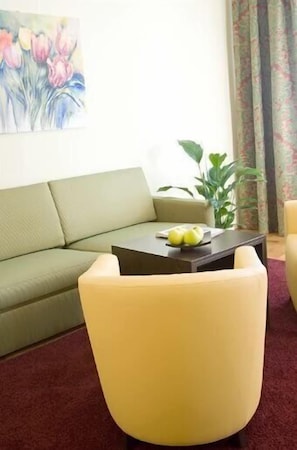 A living room with a sofa, a coffee table, and a chair. There is a painting on the wall and a plant on the side. - Appartments in der Josefstadt (Vienna)