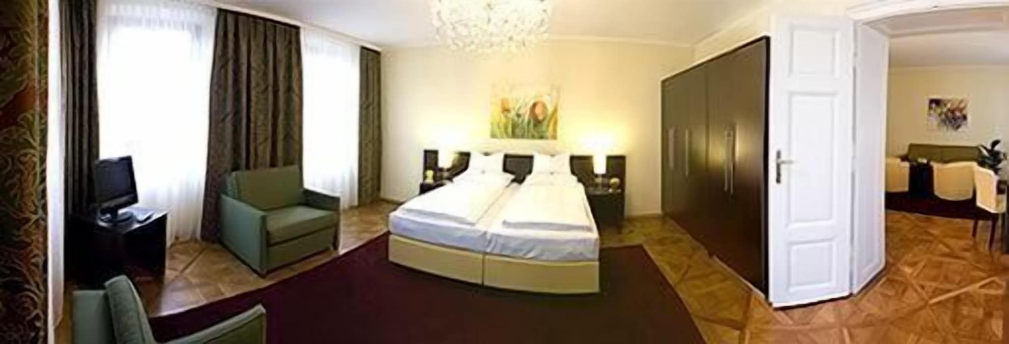 A hotel room with a large bed, a chair, a desk, and a wardrobe.